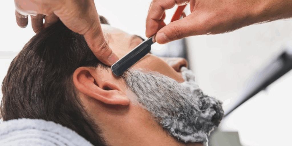 Afbeelding van een man die zijn baard laat scheren door een barbier. 